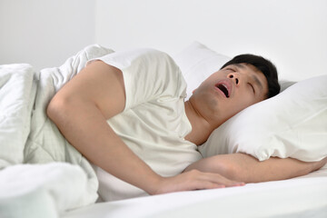 Young Asian man sleeping and snoring loudly lying in the bed.