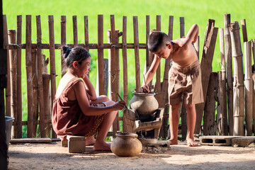 Asian children, a boy and a girl, are cooking in the kitchen of a Thai country house, where they...