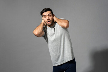 Naklejka premium Surprised young Caucasian man gasping with hands behind neck on light gray isolated studio background