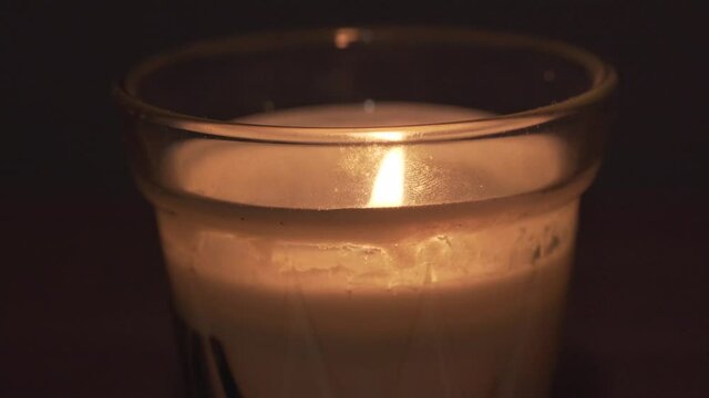 Close view of white cream candle wax in glass recipient. Bright fire flame in dark room