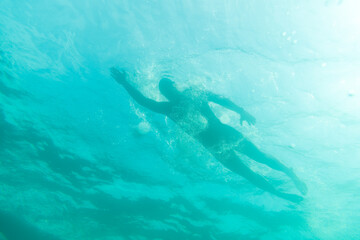 Silhouette of an athlete swimming in beautiful blue water