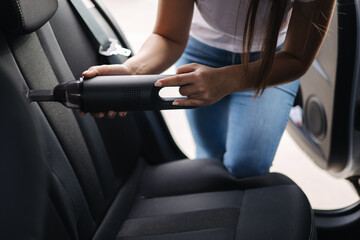 Close-up of female using portable vacuum cleaner in her car. Car interior cleaning. Woman vacuuming seats. Dust and dirt removal