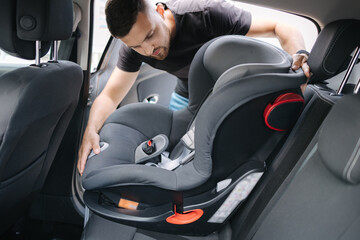 Man installs a child car seat in car at the back seat. Responsible father thought about the safety...