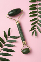 Green face roller and leaves on pink background