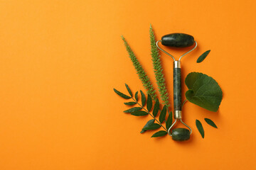 Green face roller and leaves on orange background