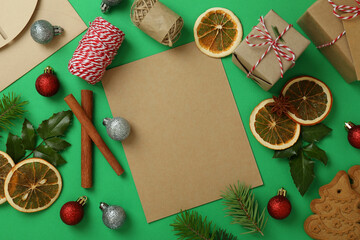 Christmas accessories and blank wishlist on green background, top view