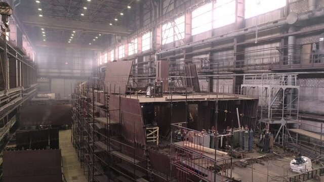 Section of restored vessel with hull made of metal sheets and high scaffolds nearby in spacious dry repairing dock