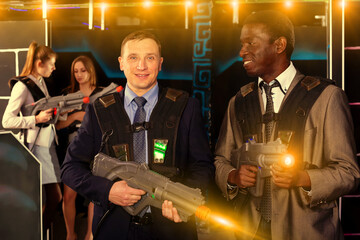 Portrait of two nice African and Caucasian men in business suits playing laser tag with co-workers