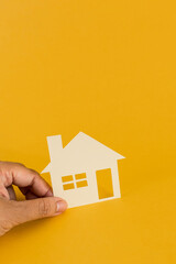 Fototapeta na wymiar Female hand holding paper house on yellow background. Family home, homeless shelter, international day of families, foster home care, family day care, social distancing, stay at home.
