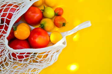 Multi-colored tomatoes in an eco-friendly bag on a yellow background. Eco shopping organic tomatoes. Choosing and buying vegetables in the store. Healthy diet