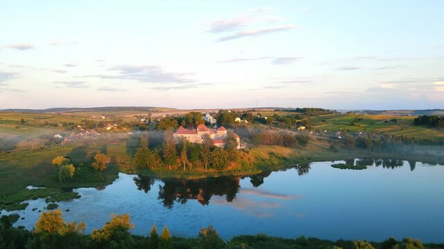 Beautiful landscape: a castle by the lake in a picturesque corner. Ancient castle in the park at sunset. Fabulous castle, sky and nature and their reflection in the lake