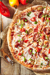 Pizza restaurant menu - Meat Pizza on parchment, topped off with meat hot sausage and pepperoni slice. Wooden table with pizza ingredients. Sunlight with harsh shadow. Rustic, natural style food.