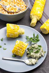 Pieces of boiled corn, sauce and spoon on gray plate.