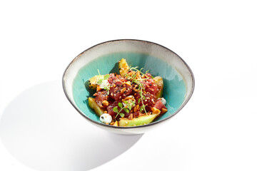 Tuna and cucumber salad bowl. Blue salad bowl isolated on white background. Salad garnished with micro greens and sesame, chopped tuna, sliced cucumber and parsley green leaf