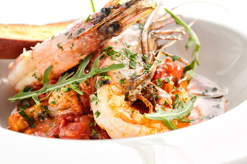 Seafood with tomato sauce on white restaurant plate. Shrimp seafood and tomato stew garnished with fried bread. Isolated on white background.