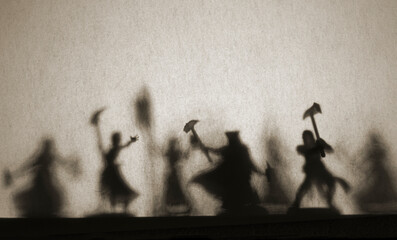 Dark silhouettes and shadows on a gray wall, figures of people with raised weapons