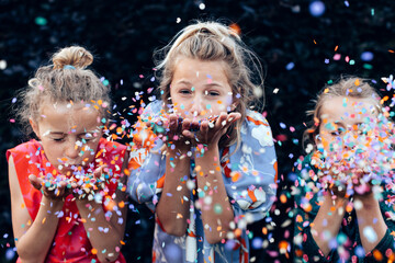 Young girls having fun celebrating while blowing confetti at party outdoor - Focus on center hands...