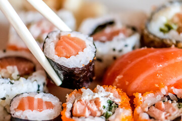 Eating various sushi. Maki, uramaki, hosomaki, sahimi and nigiri rolls set in a plate with bamboo chopsticks, close up composition