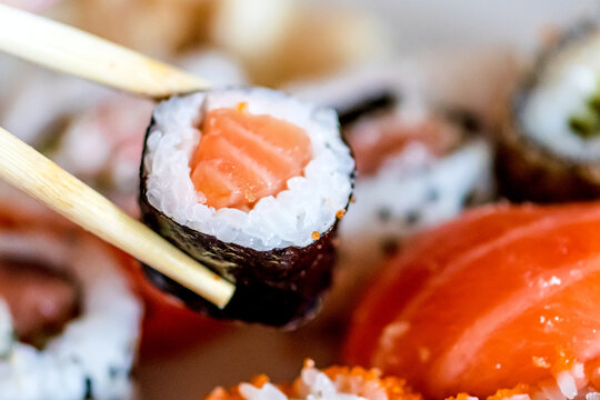 Eating various sushi. Maki, uramaki, hosomaki, sahimi and nigiri rolls set in a plate with bamboo chopsticks, close up composition