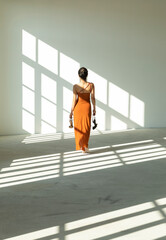 Asian girl in traditional Chinese dress walks barefoot sensually in an empty industrial building illuminated by natural sunlight