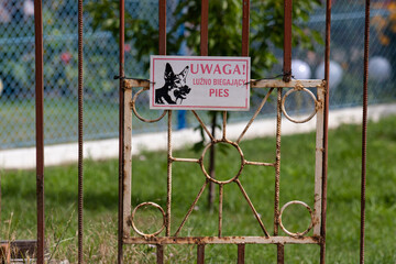 Sign at the entrance on the fence with the inscription in Polish: Attention! Loosely running dog