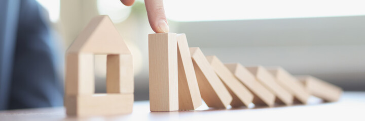 Male hand stopping falling wooden blocks in front of toy house closeup