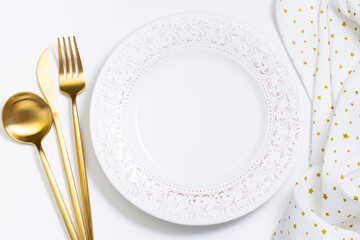 Empty white plate with ornament, golden cutlery set and napkin with stars on light background top view. Festive table setting.
