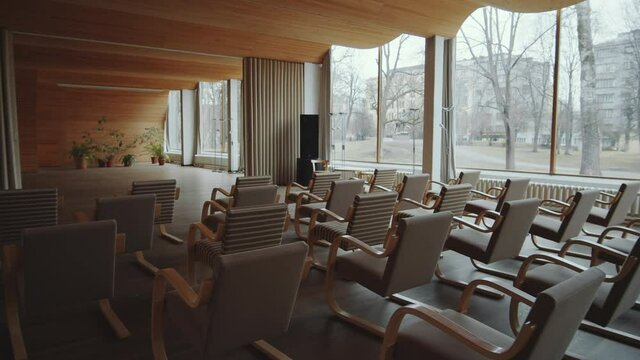 Interior of modern library auditorium with wooden wave-shaped ceiling, panoramic windows and chairs