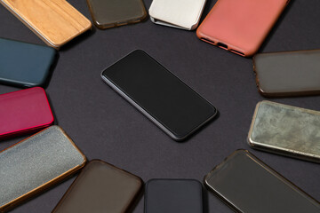 Pile of multicolored plastic back covers for mobile phones on black background with a phone on the side