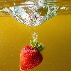 ripe strawberries fall into the water lifting splashes and air bubbles