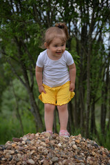 Little girl stands on pile of gravel in summer