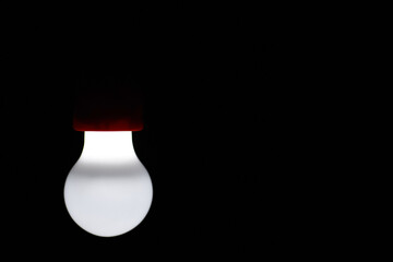 Light bulb shines on a black background, copy space