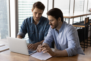 Businessmen discussing project at laptop, looking at screen, talking. Developer presenting startup to customer or investor, showing presentation on pc. Employees using computer together, sharing ideas