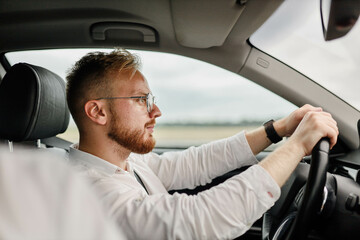 male driver with glasses driving a car, European appearance.