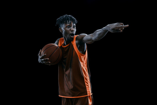 tudio shot of one professional african basketball player posing with ball isolated over dark studio background.