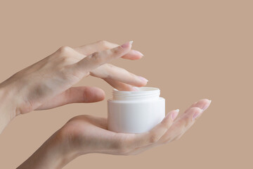 Women's fingers collect cream from round white jar. Concept of mockup for cosmetic products. Close-up, beige isolated background, copy space