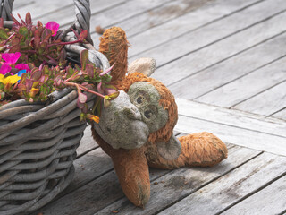 Old weathered plush monkey lies on a wooden table next to a basket of summer flowers