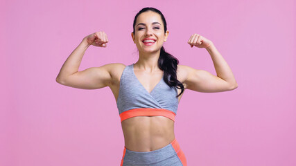 Fototapeta na wymiar joyful sportswoman showing muscles isolated on pink