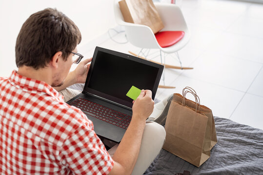 back view of man shopping on internet with laptop looking at the creadit card, black screen