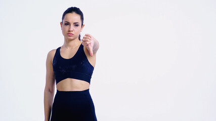 displeased young woman in sportswear showing thumb down isolated on white