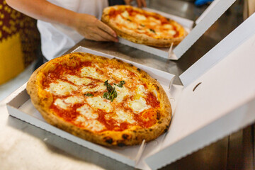 Due pizze margherita napoletane con sugo di pomodoro e mozzarella di bufala mentre vengono chiuse in due cartoni da asporto per pizze - obrazy, fototapety, plakaty