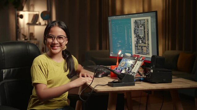 It Asian Girl Is Working With Desktop Computer And Mainboard In Home, Display Showing Cad Software. She Turns And Warmly Smiles Into The Camera, Genius Children Concept

