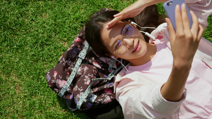 Top view of young asian woman lying on grass outdoors having video call with earphones and cellphone