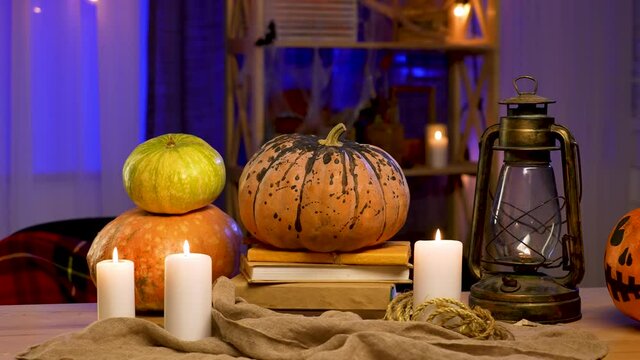 There is an oil lamp, burning candles and pumpkins on the table in the room decorated for Halloween. The background is blurred. Halloween decor. Zoom in in slow motion.
