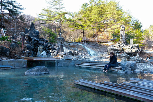 Woman sit on onzen pond surrounding of wooden pipe line in Kusatsu Onsen,Sainokawara Park hot spring ,hot water running down the valley in a warm stream in Japan.