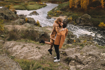 Naklejka na ściany i meble A happy couple in love in casual clothes travel together, hike and have fun in the autumn forest, enjoy nature on a weekend in fall. A man and a woman on a romantic date countryside