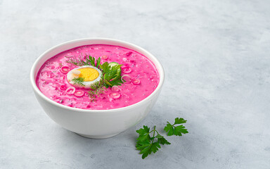 Traditional Lithuanian beetroot soup with cucumber, potatoes, beetroot, fresh herbs and kefir on a gray background.