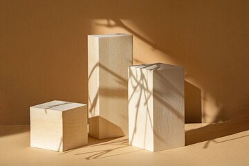 Square wooden stands, of various heights, on beige background, for demonstrating products. Shadows...