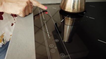 Adult woman's finger touching buttons on a ceramic hob