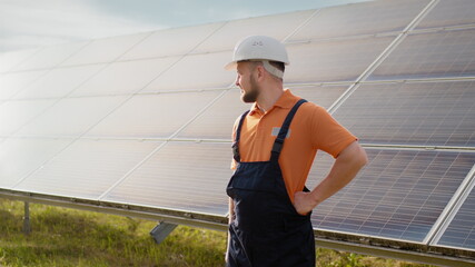 Portrait of ecological expert industrial worker in uniform standing by solar panels installation. Construction of solar station. Workman. Clean energy production. Green energy. Ecological solar farm.